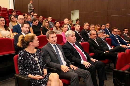 Muitas pessoas dentre homens e mulheres estão sentadas nas poltronas vermelhas do Auditório Pleno do TJ.