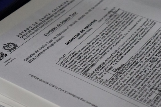 A imagem mostra um documento impresso em cima de uma mesa branca, no papel está escrito "certidão de inteiro teor" e "registro de imóveis". O papel está assinado.