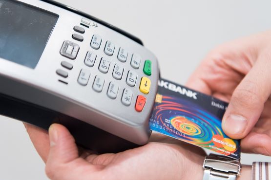 A imagem mostra as mãos de uma pessoa segurando uma máquina de cartão cinza, com um cartão colorido sendo inserido.